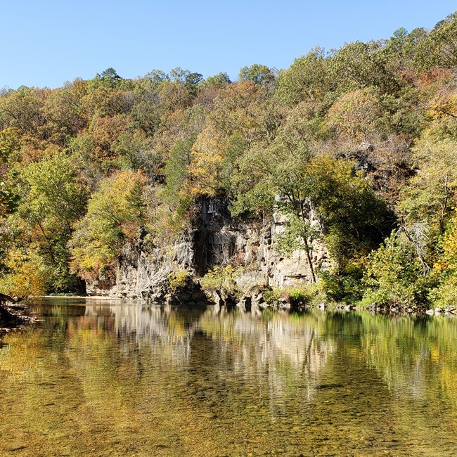A wide, shallow river flows in the foreground with tall bluffs in the background.