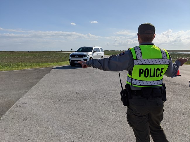 A person wearing a reflective vest that says Police. They are directing traffic.