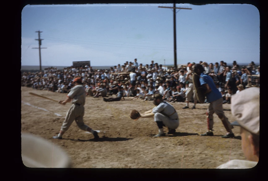 A crowd watches a man swing his bat in a live baseball game. A crowd watches a live baseball game.