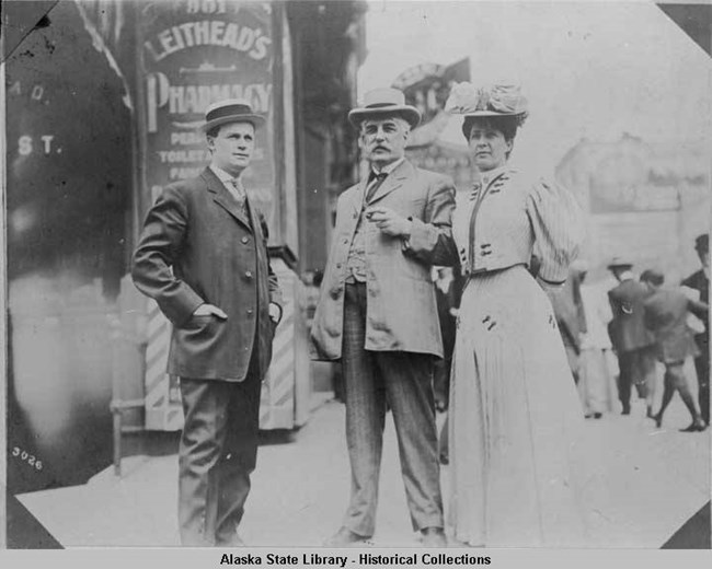 A black and white photo of Annie Hall Strong standing next to two men on her right.