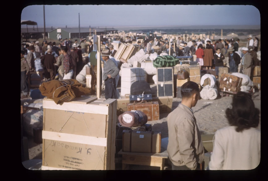 A crowd of people carrying suitcases and other items to the incarceration camps. A crowd of people carrying suitcases and other items.