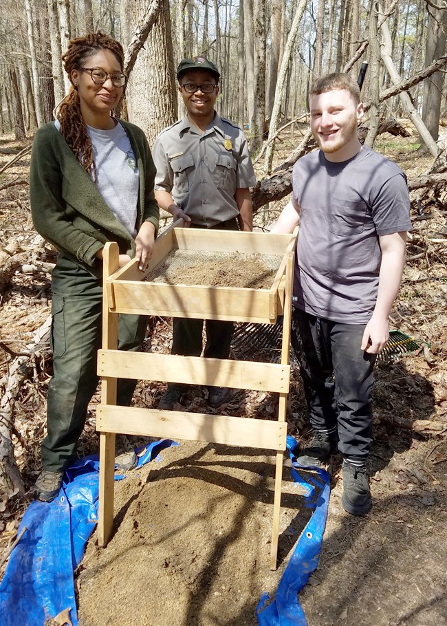 Two park employees stand with a volunteer around a screen unit, to survey materials from tree falls on the Eastern Front.