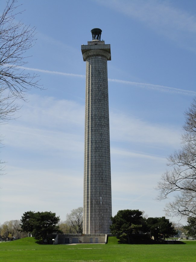 the east aspect of  Perrry's Victory Memorial clouds streak a blue sky and green grass in foreground