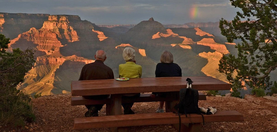Viewing Grand Canyon Sunset Three people sitting at a picnic table watching sunset and a rainbow over the Grand Canyon