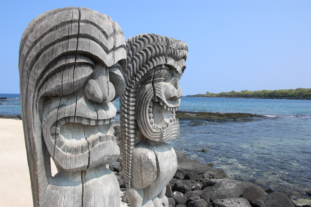 Two carved kiʻi images look out over the ocean