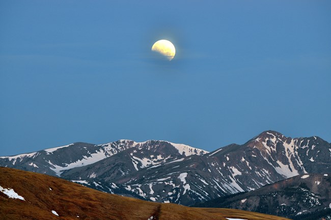 Moon rising over mountain peaks in summer