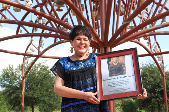 Lady standing outside holding a framed image of her ancestor.