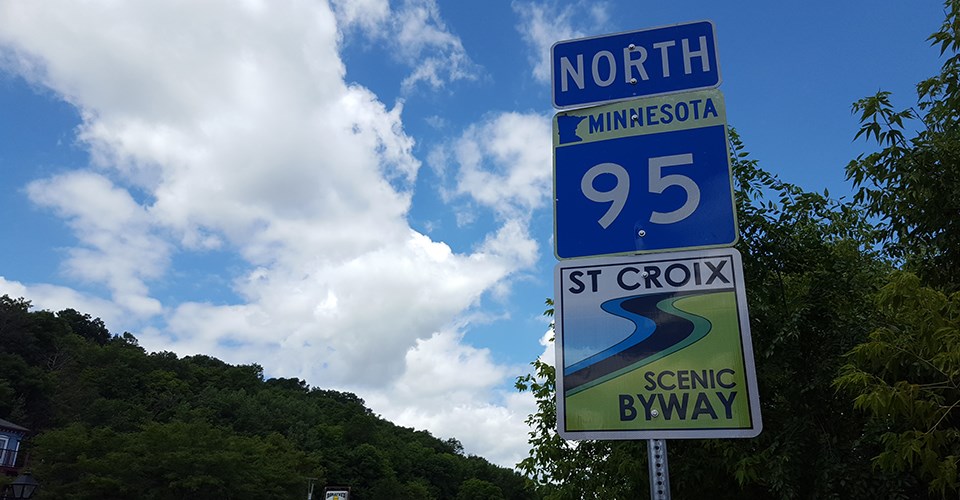 A blue highway sign with white letters and numbers over a green and white sign against a blue sky.