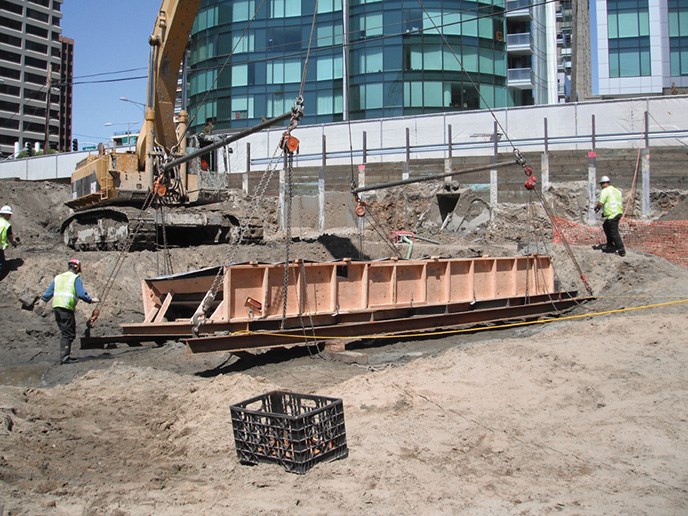 A large machine uses chains to lift a wooden case containing an old wooden boat.