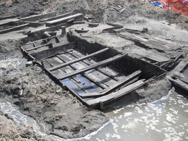 Old rectangular-shaped wooden boat sitting in the mud.