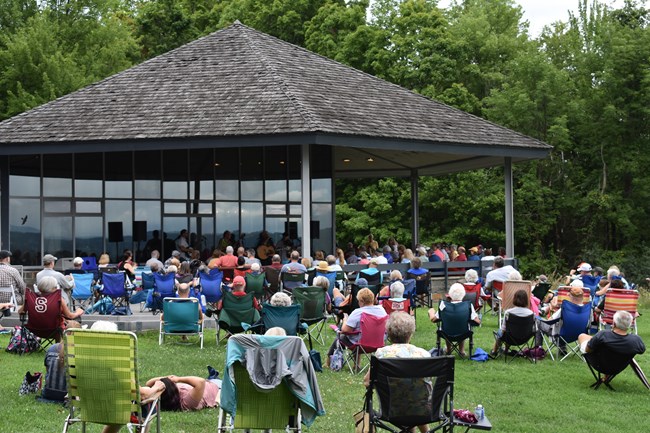 A large group seated in lawnchairs watches a band of musicians