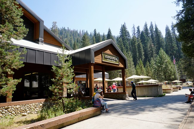 Guests sit outside on picnic tables in front of a large brown and green building.