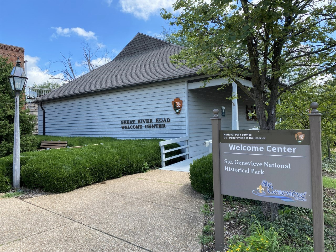 A blue windowless building with a sign on the right. Sign states "Welcome Center."