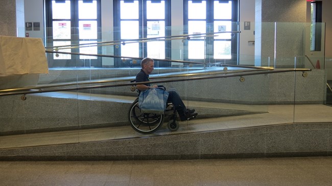 A visiting in a wheelchair is using the inside ramp to go outside onto the Fort Wood level of the monument.