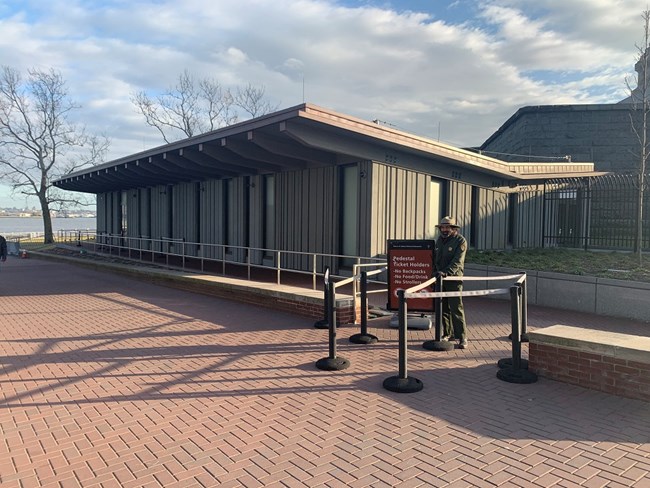 The secondary screening building is a gray building which a park ranger is standing in front of