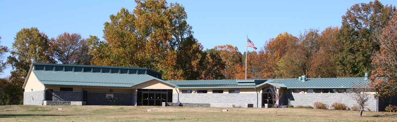 A grey stone building with a green roof and American flag flying behind it.