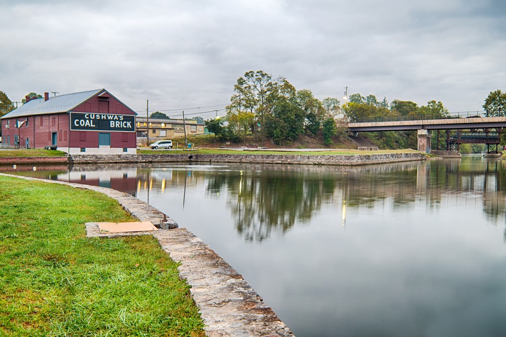 A warehouse with "Cushwa's Coal Brick" painted on the side stands next to a wide basin of water, edged by stone walls and turf.