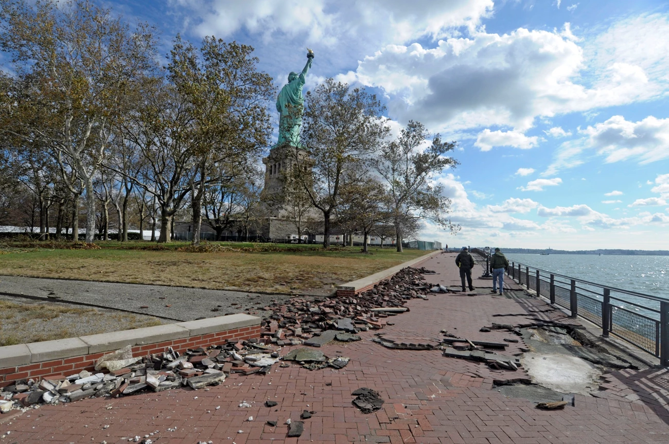 STLI Liberty Island storm damage Broken bricks from storm damage are scattered along a walkway with the Statue of Liberty in the background