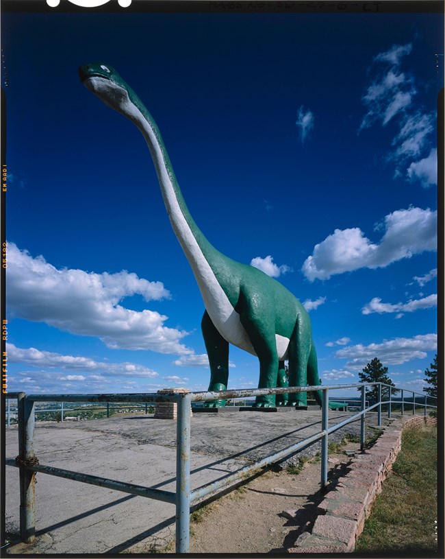 Green and white Apatosaurus statue with blue sky and fluffy clouds in background