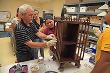 A man shows four other people how to repair a wooden table