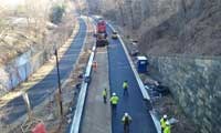 workers in fluorescent vests pave road with stone wall on right