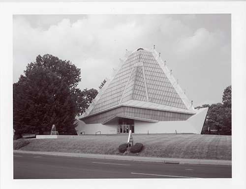 a glazed, pyramidal tower, broad in form and made up of three sides, and a base of reinforced concrete, steel, and glass