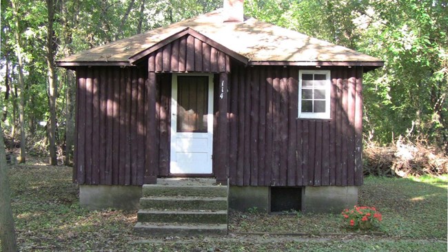 100002106-Lorine Niedecker Cottage A simple 20 foot by 20 foot, single story, wood frame building with painted split-log vertical sidin