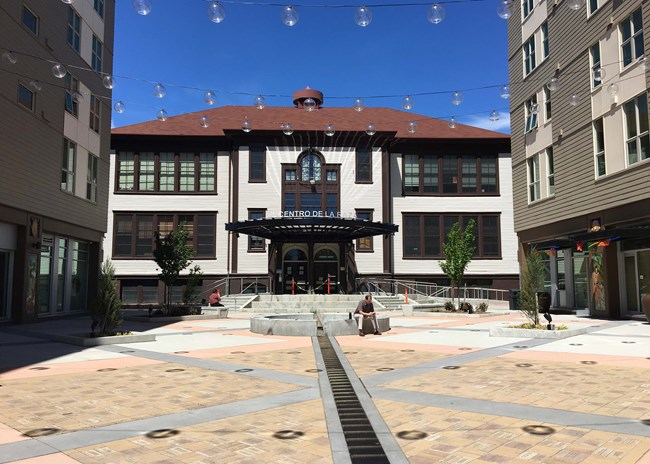 Entrance to a two story building with large windows on both wings. An awning reading “El Centro de la Raza” is above doors.