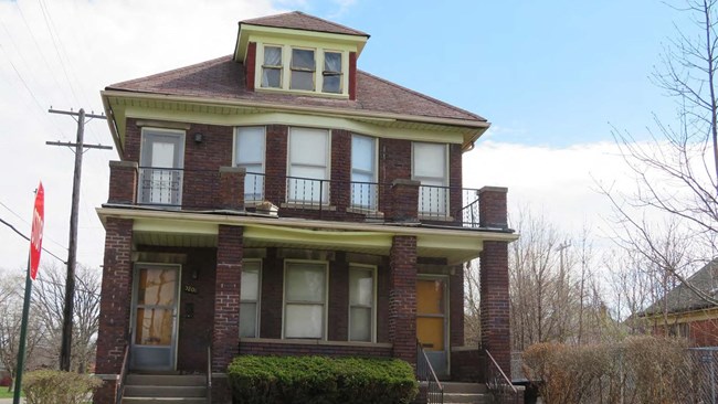 Parks, Rosa L. (McCauley) and Raymond, Flat A two-and-one-half story Craftsman style brick building with asphalt shingles, with a porch