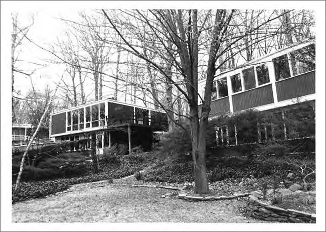 Image of two modern houses, trees, and grass.