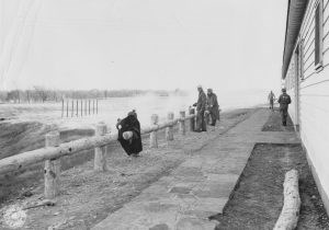 Work Detail Five men gray uniforms one with letters PW on back of shirt building a thick rail fence.