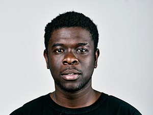 A dark-skinned man in a black t-shirt staring at the camera