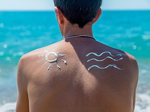 a man with sunscreen art on his back looks at a turquoise ocean