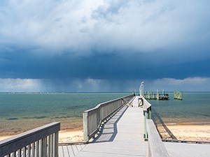 Gray dock overlooking a blue ocean with storm clouds rolling in