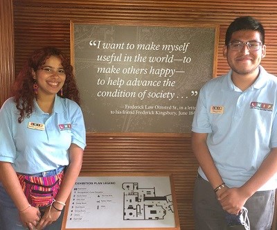 two interns posing in front of a frederick law olmsted sign