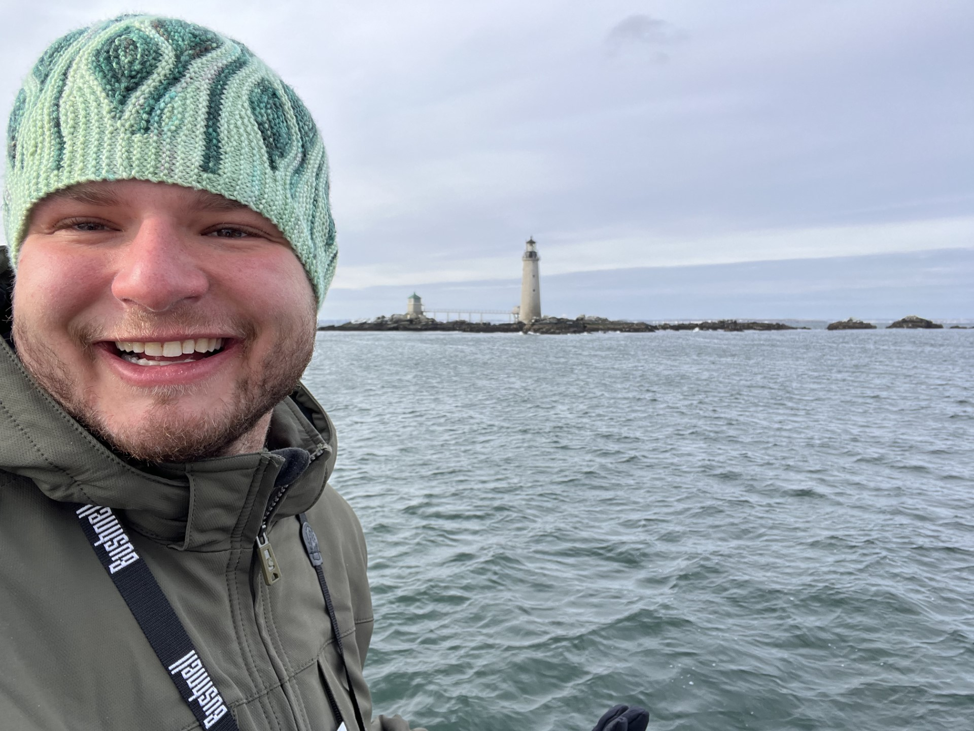 A male wearing a beanie hat is smiling with water in the background