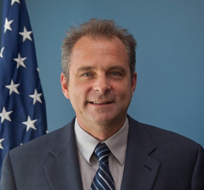 A man smiling with American flag in the background