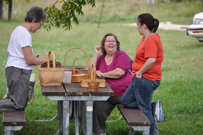 3 visitors lay out baskets on a table at a picnic area.