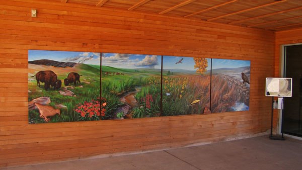 Mural outside the visitor center door shows prairie life, including bison, prairie chickens, grasses, sky, hills, plants, and other birds.