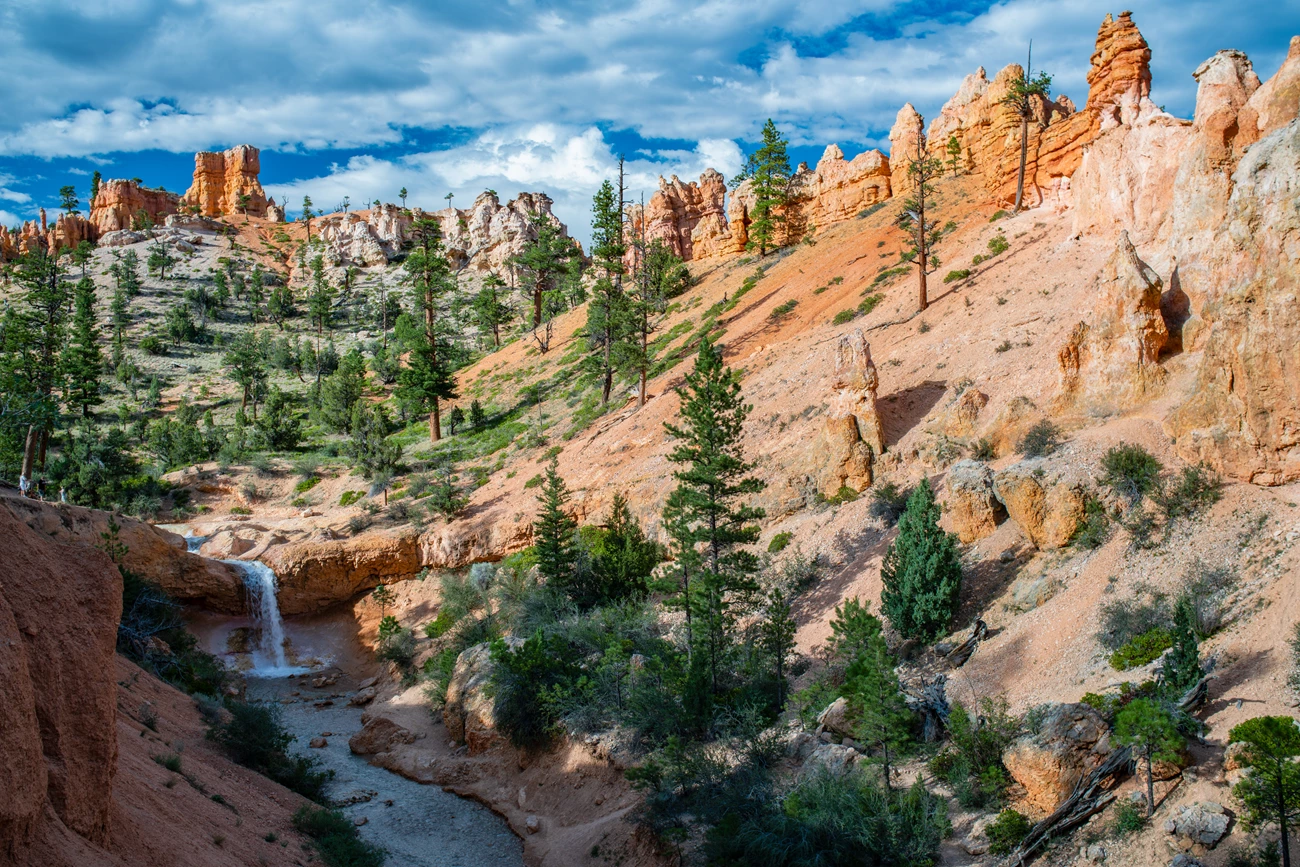 Mossy Cave An overview of a stream flowing through red rocks with a waterfall in the distance