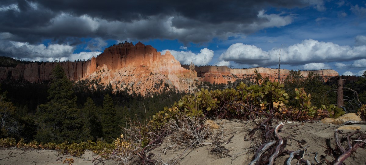 A large land formation with irregular red rock structures under dark storm clouds