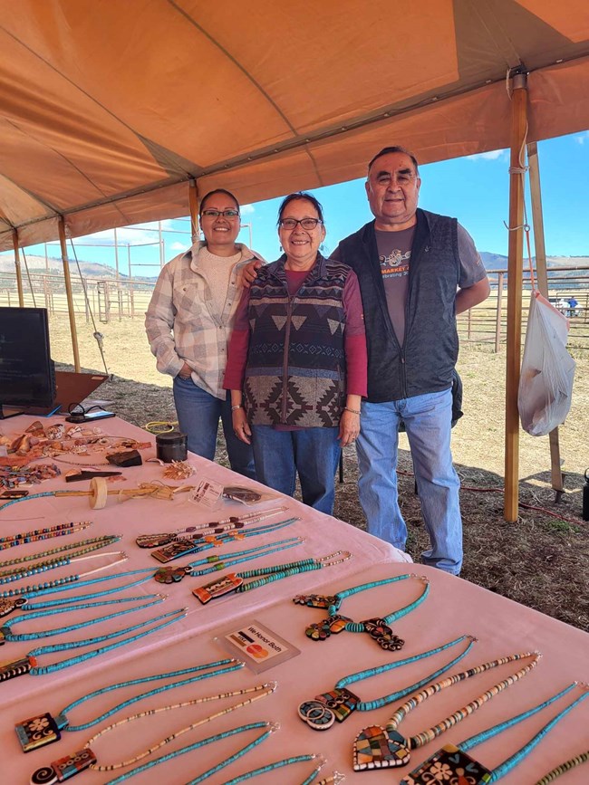 Three jewelry makers stand together behind a table full of their hand-made jewelry.