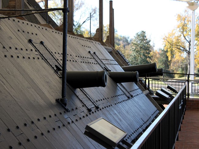 Side view of the gunboat with several cannons pointing out from the interior of the ship