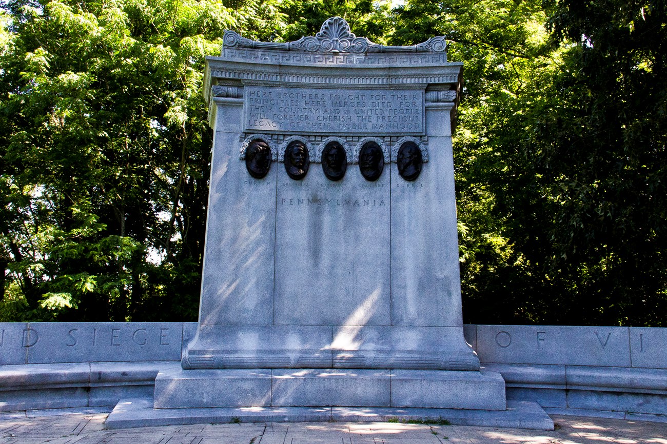 A tall granite slab with a short inscription on top and five small bronze relief portraits.