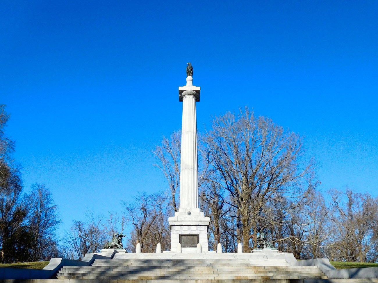 Stairs lead up to a tall column with a statue of an eagle perched at the top.