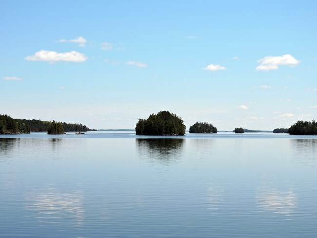 A large, blue, scenic lake reflects images of several islands and clouds.