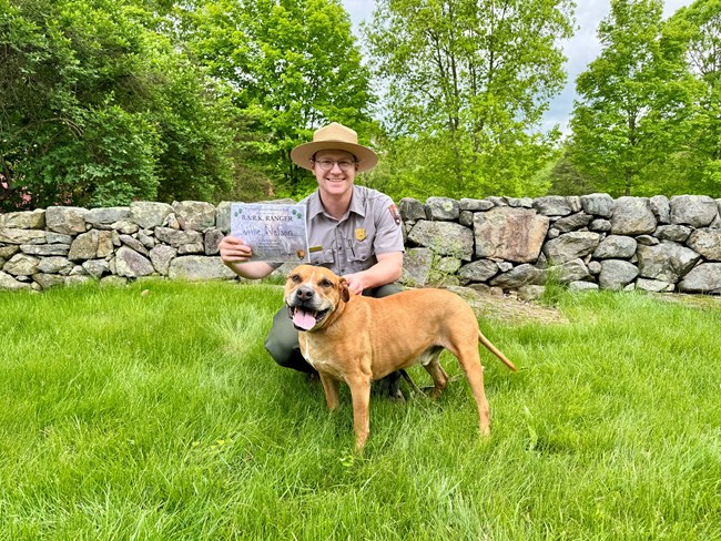 A Ranger holding a B.A.R.K. Ranger certificate behind a dog