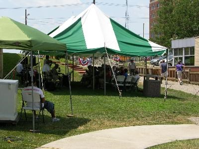 Two tents with several people sitting under them on the lawn of park buildings.