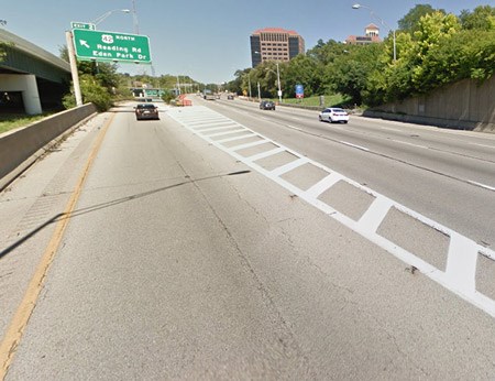 A green street sign above the highway with a large concrete wall on left