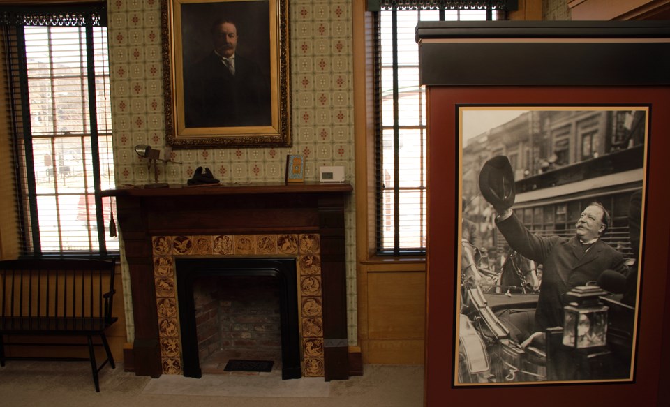 Framed photos of a man with a wide mustache wearing a suit, the black and white photo shows him raising his hat up in the air